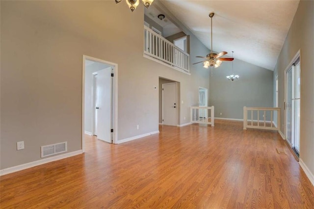 unfurnished living room with ceiling fan with notable chandelier, high vaulted ceiling, and light hardwood / wood-style floors