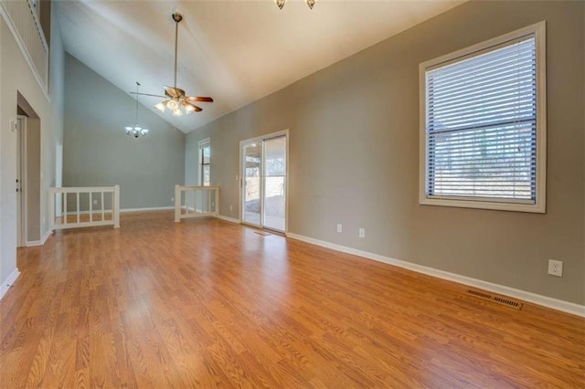 spare room featuring high vaulted ceiling, ceiling fan with notable chandelier, and light wood-type flooring