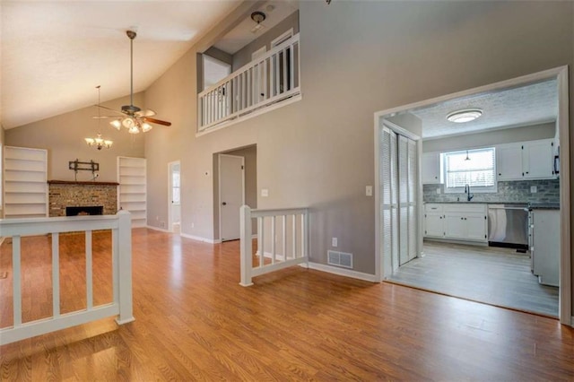 kitchen featuring a brick fireplace, stainless steel dishwasher, white cabinets, and light wood-type flooring