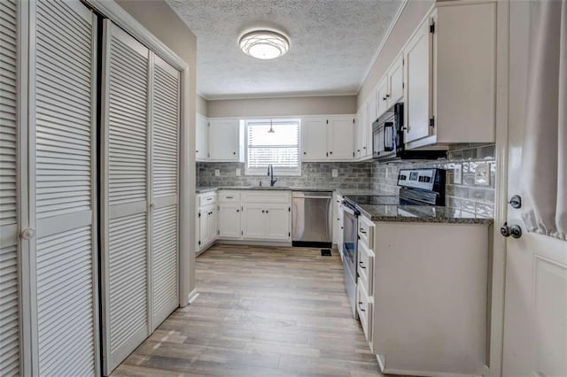 kitchen featuring light hardwood / wood-style flooring, appliances with stainless steel finishes, white cabinetry, dark stone countertops, and decorative backsplash