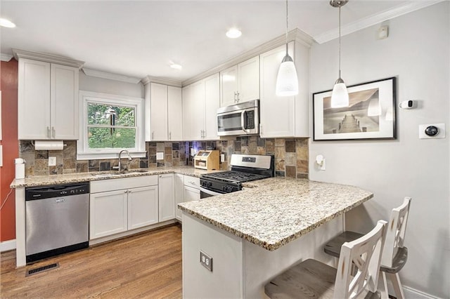 kitchen with appliances with stainless steel finishes, a sink, light wood-style flooring, a peninsula, and ornamental molding