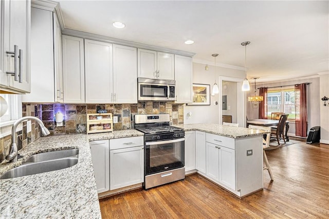 kitchen with wood finished floors, a sink, a peninsula, an inviting chandelier, and stainless steel appliances