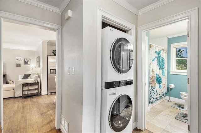 clothes washing area featuring stacked washing maching and dryer, baseboards, ornamental molding, and laundry area