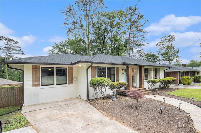 ranch-style home featuring covered porch, brick siding, fence, and roof with shingles