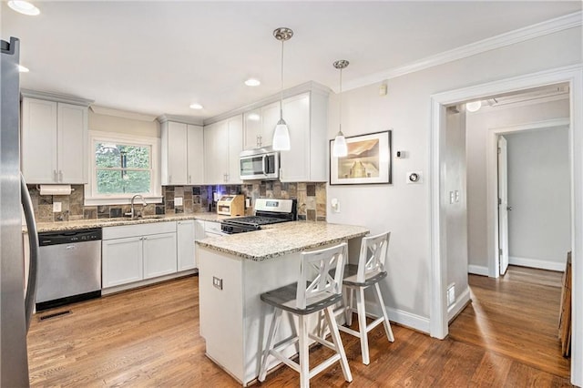 kitchen with a sink, appliances with stainless steel finishes, a peninsula, and ornamental molding