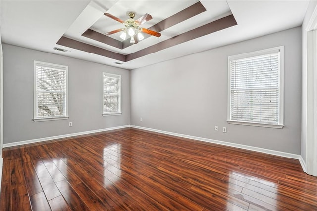 empty room with a tray ceiling, hardwood / wood-style flooring, a ceiling fan, and visible vents