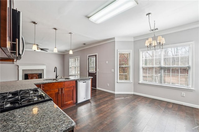 kitchen featuring a brick fireplace, dark wood-type flooring, ceiling fan with notable chandelier, appliances with stainless steel finishes, and a sink