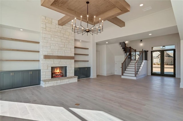 unfurnished living room with a stone fireplace, a chandelier, hardwood / wood-style flooring, beam ceiling, and a high ceiling
