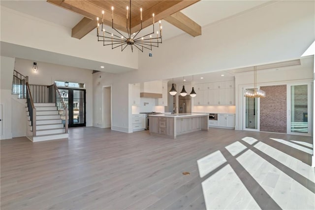 unfurnished living room with beam ceiling, light hardwood / wood-style floors, a high ceiling, and a notable chandelier