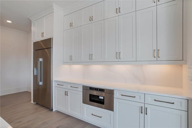 kitchen featuring white cabinets, backsplash, built in appliances, crown molding, and light hardwood / wood-style flooring