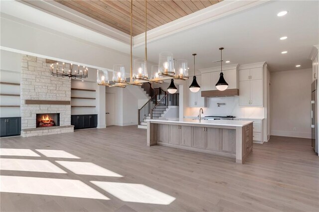 kitchen with a spacious island, a stone fireplace, hanging light fixtures, light wood-type flooring, and a tray ceiling