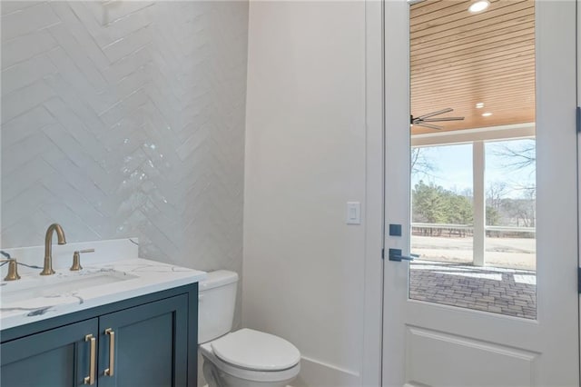 bathroom with ceiling fan, vanity, toilet, and tile walls