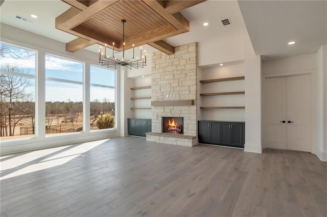 unfurnished living room with a stone fireplace, a chandelier, light hardwood / wood-style floors, and beam ceiling