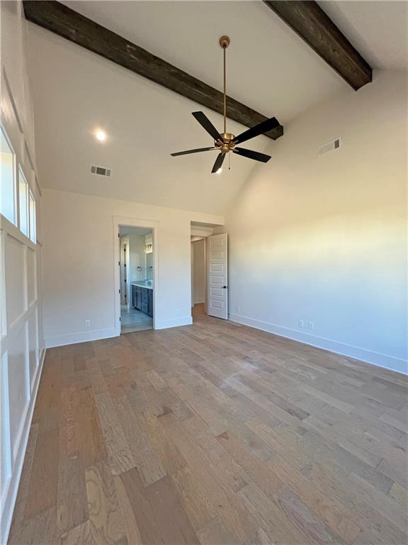 unfurnished bedroom with light wood-type flooring, ceiling fan, high vaulted ceiling, beam ceiling, and ensuite bathroom