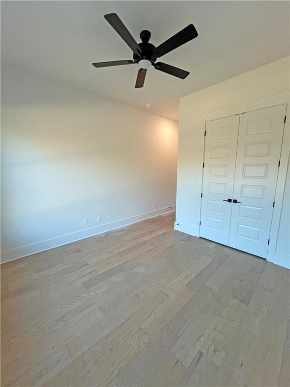 unfurnished bedroom with light wood-type flooring, ceiling fan, and a closet