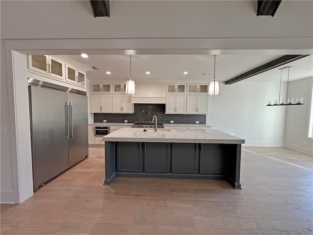 kitchen with white cabinetry, beamed ceiling, built in refrigerator, an island with sink, and hanging light fixtures