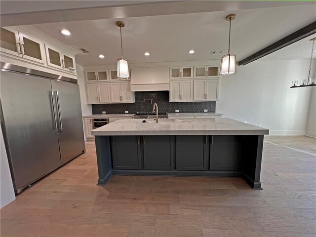 kitchen with hanging light fixtures, white cabinetry, built in fridge, and an island with sink