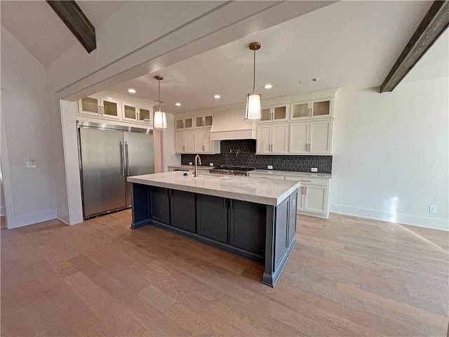 kitchen with custom exhaust hood, pendant lighting, a center island with sink, white cabinetry, and stainless steel built in refrigerator