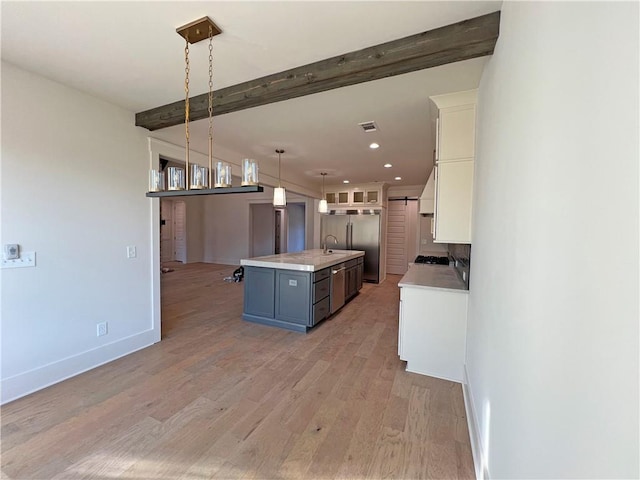 kitchen featuring hanging light fixtures, an island with sink, beamed ceiling, white cabinets, and light hardwood / wood-style flooring