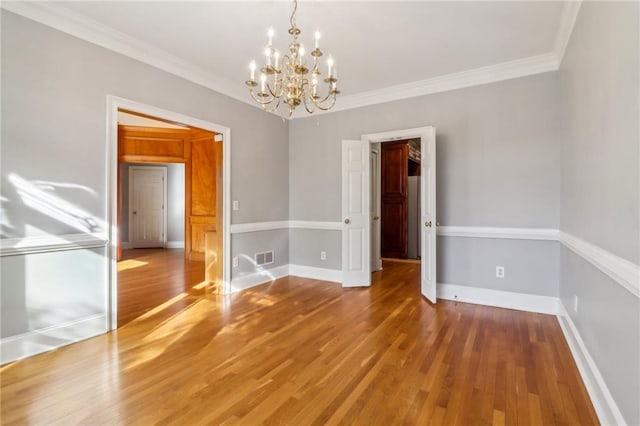 empty room featuring wood-type flooring, crown molding, and an inviting chandelier