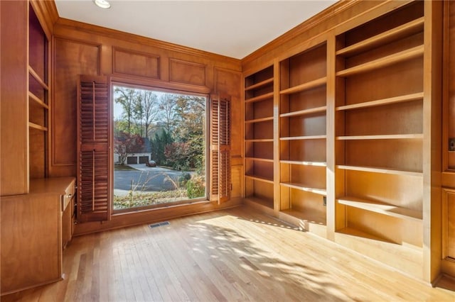 unfurnished room featuring built in shelves, wood walls, and light hardwood / wood-style floors