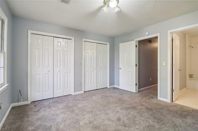 unfurnished bedroom featuring two closets, light carpet, and ensuite bath