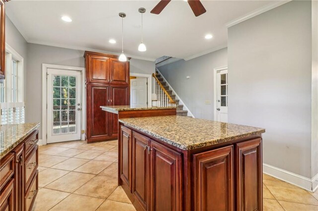 kitchen with a center island, crown molding, light stone countertops, light tile patterned floors, and decorative light fixtures