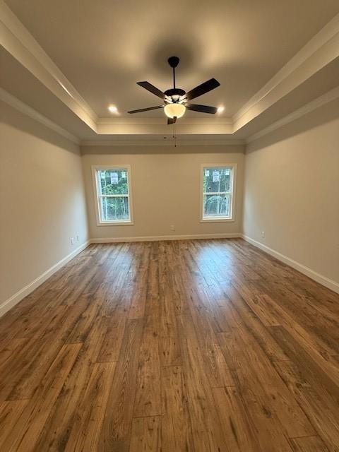 spare room featuring a raised ceiling, healthy amount of natural light, dark wood-type flooring, crown molding, and recessed lighting