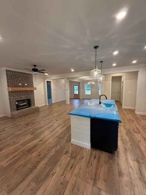 kitchen featuring a sink, crown molding, a ceiling fan, wood finished floors, and a fireplace