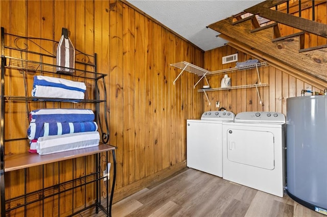 laundry area featuring separate washer and dryer, a textured ceiling, wooden walls, hardwood / wood-style floors, and water heater