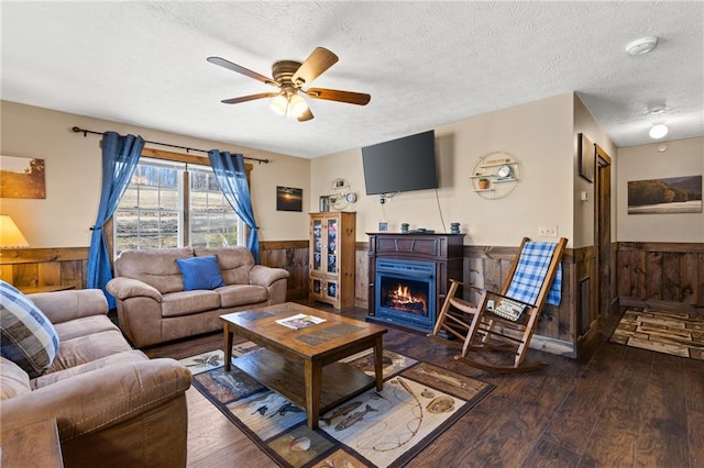 living room featuring ceiling fan, dark wood-type flooring, a textured ceiling, and wooden walls