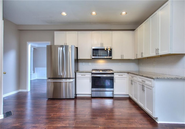 kitchen featuring appliances with stainless steel finishes, backsplash, dark wood-type flooring, light stone countertops, and white cabinets