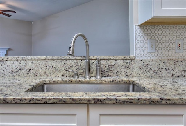 interior details with ceiling fan, sink, white cabinets, and tasteful backsplash