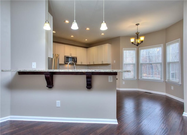 kitchen with light stone countertops, appliances with stainless steel finishes, a kitchen bar, hanging light fixtures, and dark hardwood / wood-style floors