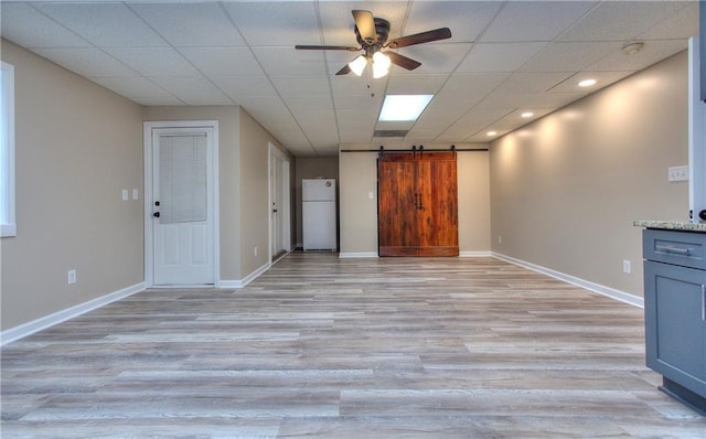 interior space featuring light wood-type flooring, ceiling fan, a barn door, and a drop ceiling