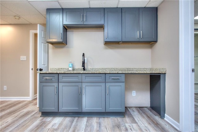 kitchen featuring light hardwood / wood-style floors, a drop ceiling, and light stone countertops