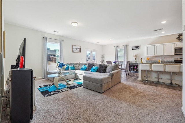 living room with light wood-style floors, visible vents, and light colored carpet