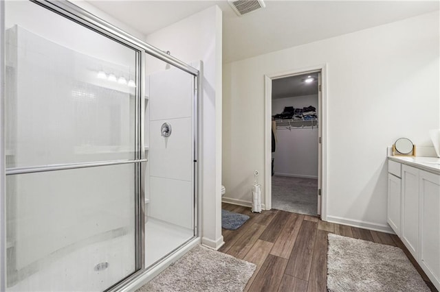 bathroom featuring toilet, wood finished floors, vanity, visible vents, and a stall shower