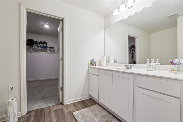 bathroom with visible vents, baseboards, wood finished floors, a walk in closet, and vanity