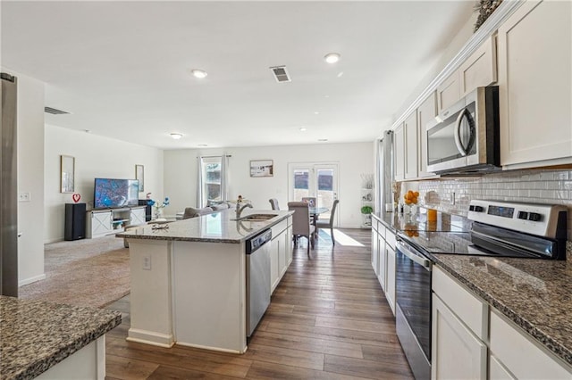 kitchen with visible vents, dark stone counters, open floor plan, stainless steel appliances, and backsplash