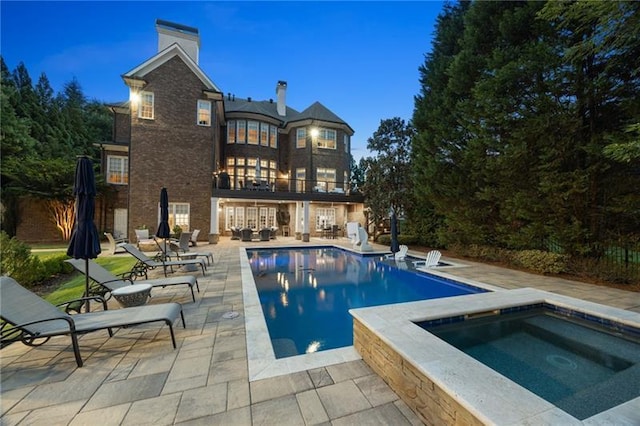 pool at dusk featuring a patio area and an in ground hot tub