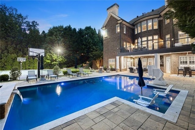 pool at dusk featuring pool water feature and a patio area