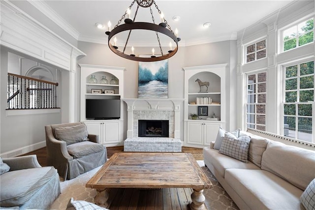 living room featuring an inviting chandelier, hardwood / wood-style floors, ornamental molding, a brick fireplace, and built in shelves