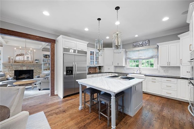 kitchen featuring white cabinets, hanging light fixtures, a stone fireplace, and stainless steel built in refrigerator