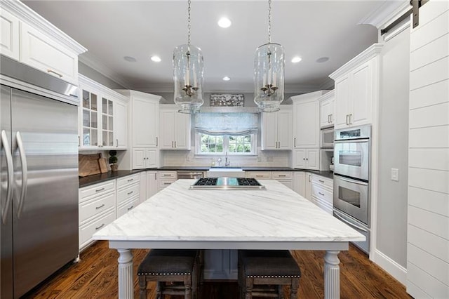 kitchen with built in appliances, white cabinetry, decorative backsplash, hanging light fixtures, and a barn door