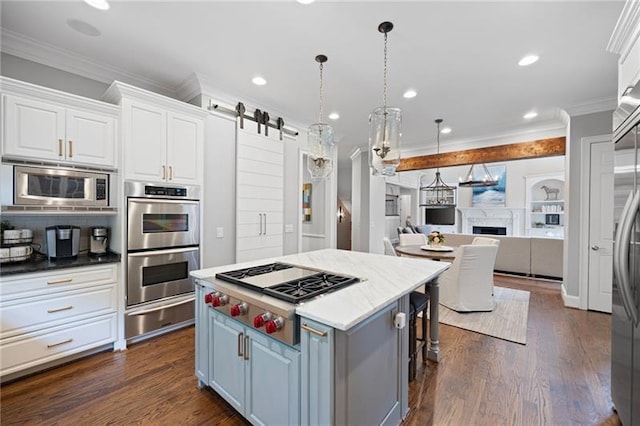 kitchen with a barn door, appliances with stainless steel finishes, ornamental molding, a kitchen island, and white cabinetry