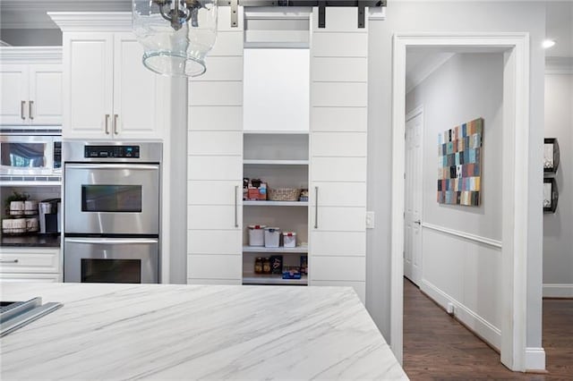 kitchen with stainless steel appliances, white cabinetry, light stone counters, a barn door, and crown molding