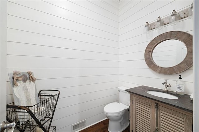 bathroom with toilet, vanity, and wood walls