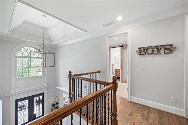 hallway with a notable chandelier, a tray ceiling, crown molding, a barn door, and wood-type flooring