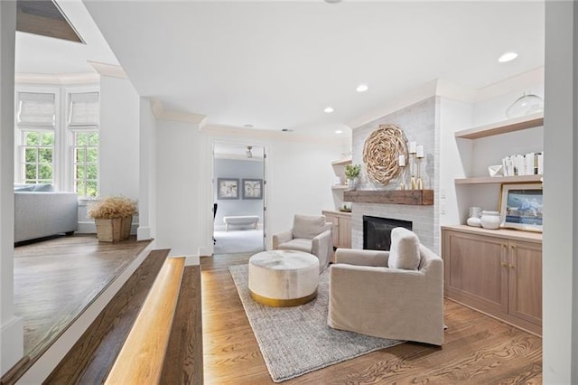 living room with a fireplace, built in features, ornamental molding, and hardwood / wood-style floors